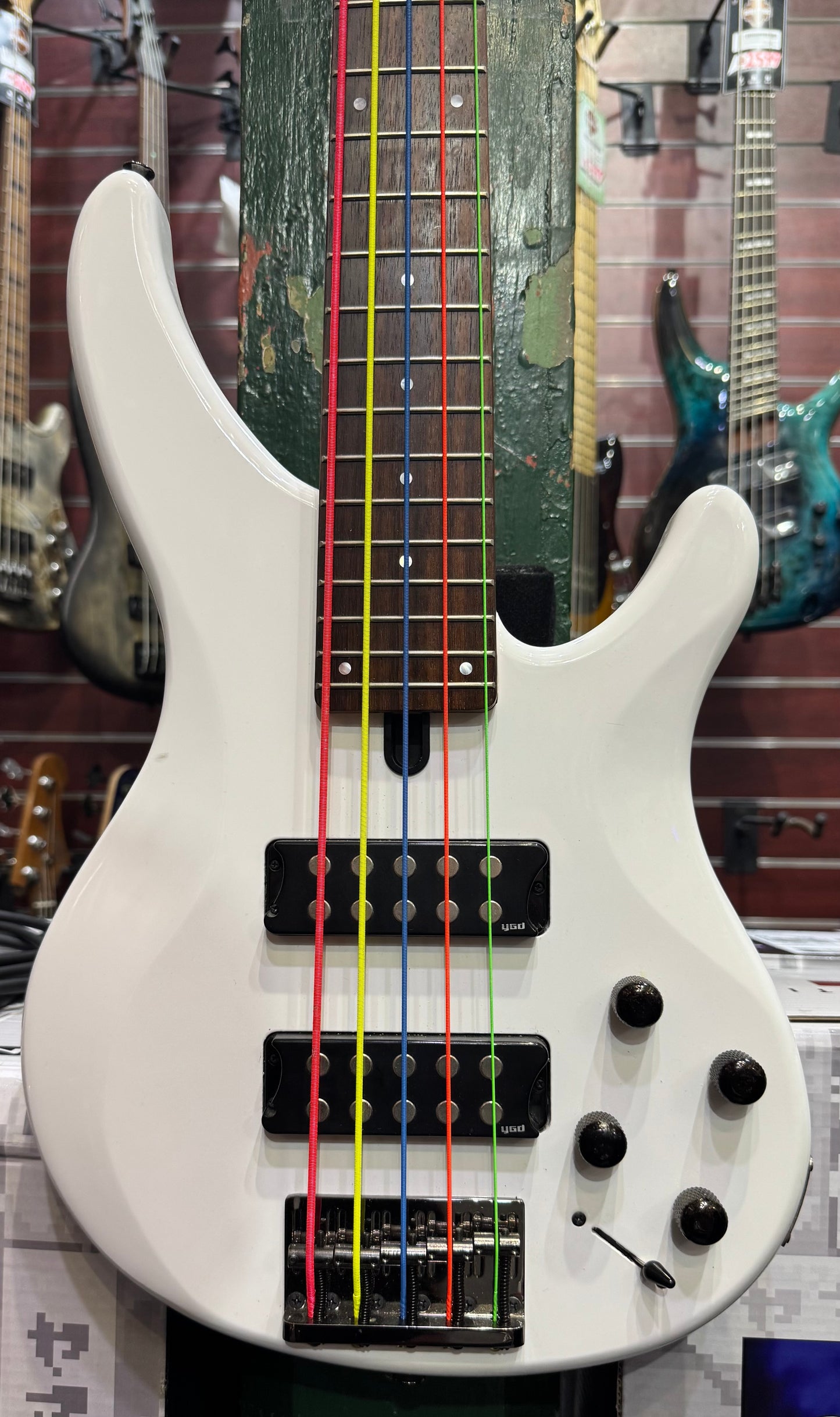White bass guitar with colorful strings on a blurred background of other guitars
