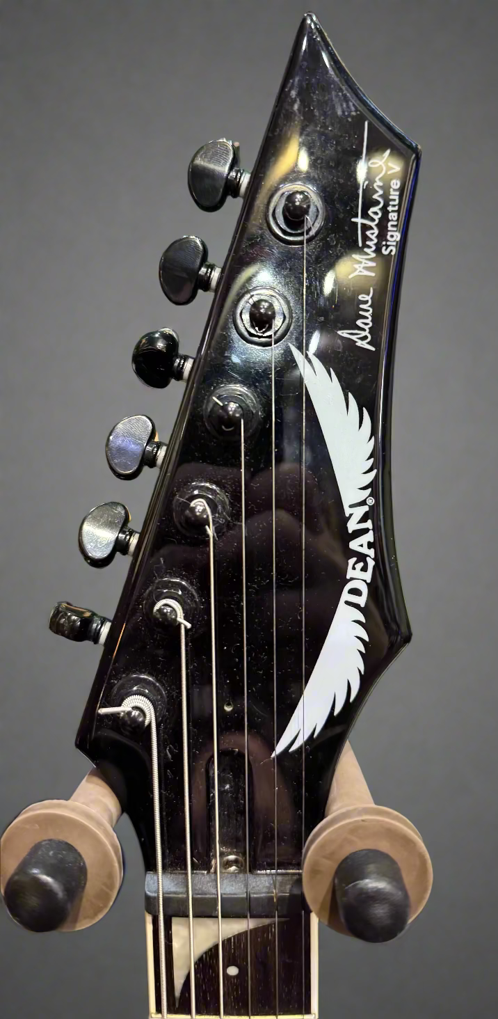 Close-up of a Dean guitar headstock with brand logo on a green background