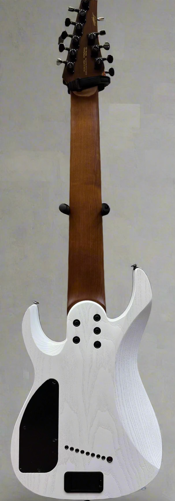 White electric guitar body with a brown neck against a background of amplifiers and guitars.