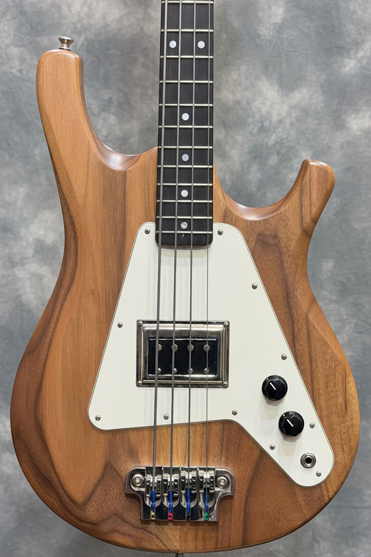 Wooden bass guitar with a white pickguard against a guitar rack background