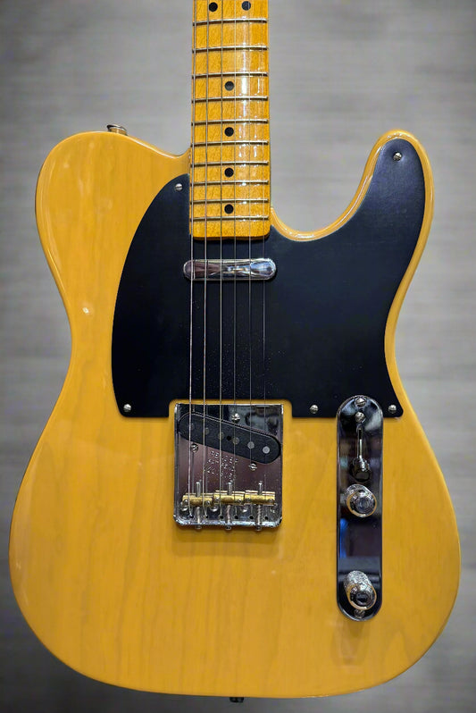 Yellow electric guitar with black pickguard on a blurred background of other guitars