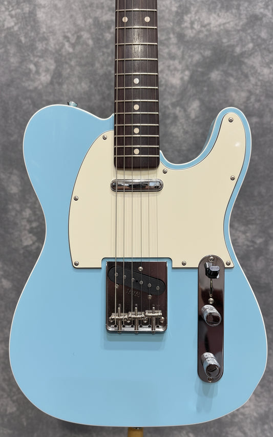 Light blue electric guitar with cream pickguard against a blurred background of other guitars