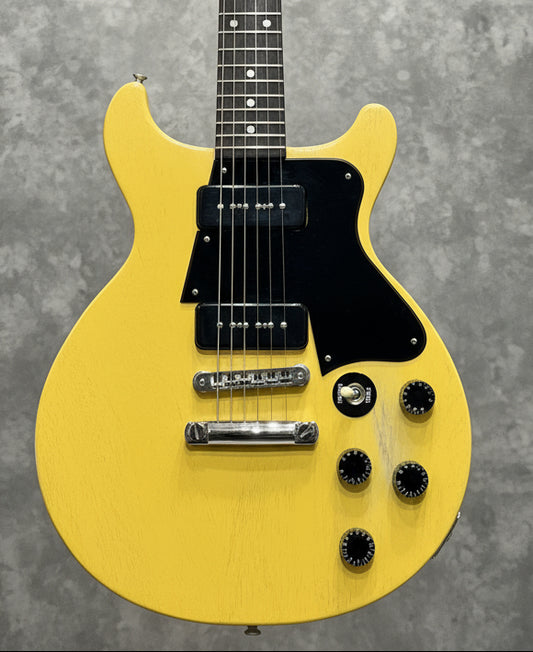 Yellow electric guitar with a black pickguard on a guitar rack.