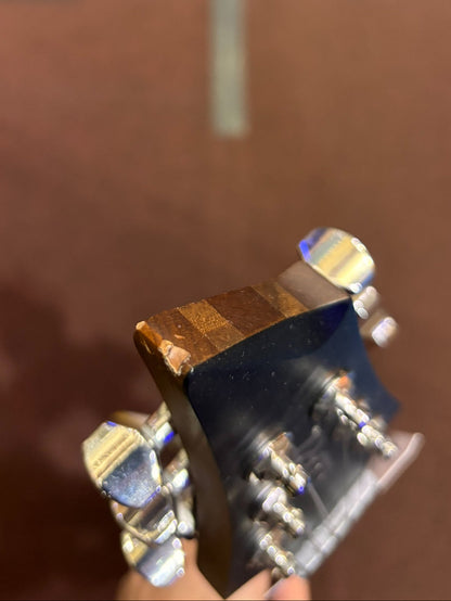Close-up of a guitar neck with a brown finish and silver tuning pegs against a blurred background.