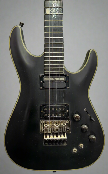 Black electric guitar with green pickguard against a brick wall background